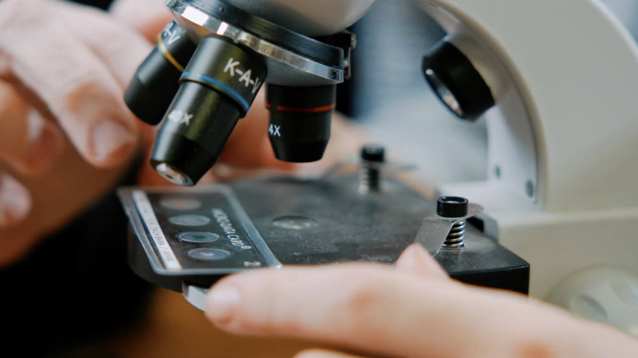 Two hands placing a slide on a microscope. 